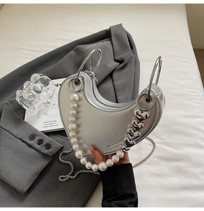 Dettaglio borsa a cuore argento con manico di perle e metallo su un blazer grigio