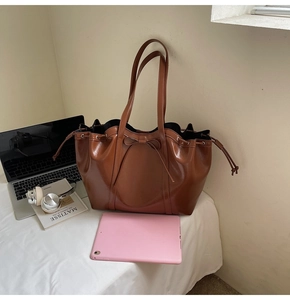 Detail of brown leather tote bag featuring a decorative bow and drawstring closure
