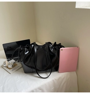 Large black glossy tote bag with drawstring closure showing laptop and tablet storage