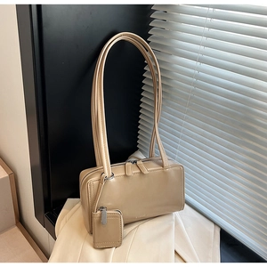 Detail of minimalist beige baguette bag with double zipper and mini pendant charm