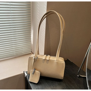 Detail of beige shoulder bag with dual straps, silver hardware and a small square pendant