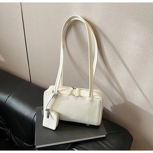 Detail of cream baguette bag with dual shoulder straps and a mini matching zipper pouch