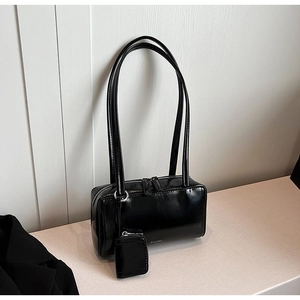 Detail of minimalist black glossy leather baguette bag with dual straps and mini pouch