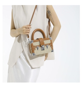 Detail of a woven box bag with brown leather trim and metallic corner protectors