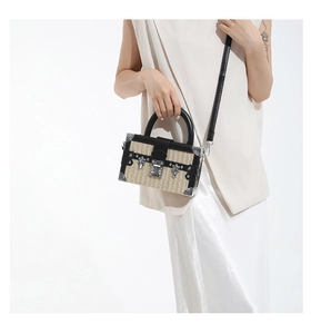 Detail of a straw-woven box bag with black leather trim and silver metal corners