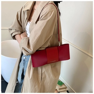 Detail of red leather baguette bag with bow design and thin shoulder strap worn on person