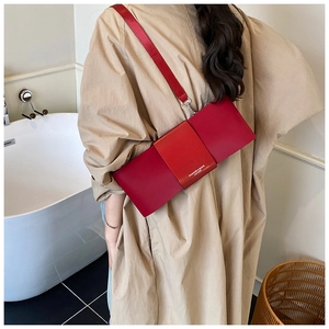 Detail of red leather baguette bag with strap worn by a model in a minimalist room