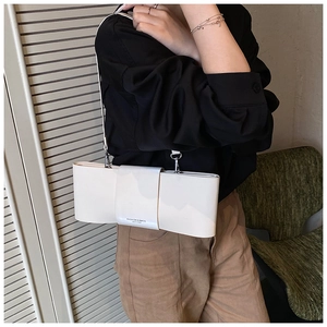 Detail of cream-white bow-shaped patent leather shoulder bag with fine silver buckle strap