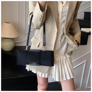 Detail of minimalist black baguette bag with bow-like structure and fashion text on the side