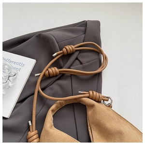 Detail of camel suede handbag featuring a braided knot strap and silver hardware accents
