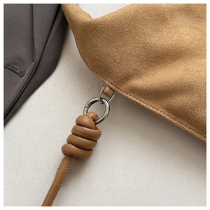 Macro shot of tan suede handbag showing silver ring hardware and knotted strap stitching