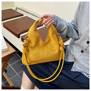 Close-up of yellow suede dumpling bag with integrated handle and knotted rope shoulder strap