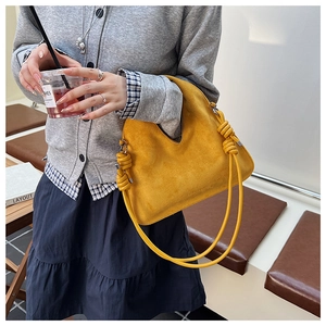 Detailed view of yellow suede handbag featuring V-shaped opening and decorative rope knots