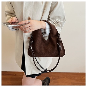 Close-up of dark brown suede shoulder bag featuring a unique knotted handle and metal hardware