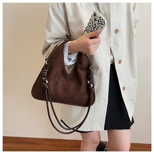 Detail of dark brown suede handbag featuring knotted rope handle and silver metal buckle