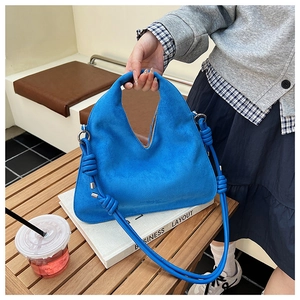 Close-up of blue suede hobo bag with a decorative knotted shoulder strap on a table
