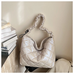Macro shot of beige quilted puffer tote featuring gathered handle and silver metal zipper
