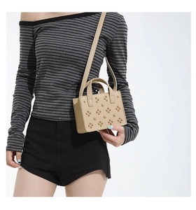 Sac bandoulière beige à rivets avec texture cuir porté par un mannequin féminin