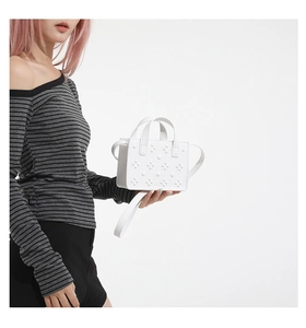 Gros plan d'un sac à bandoulière blanc clouté montrant la texture et la poignée en métal