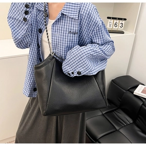 Détail d'un sac cabas en cuir grainé noir avec bandoulière chaîne porté par un mannequin