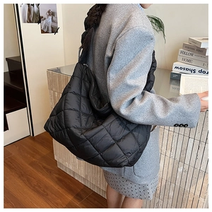 Detail of black quilted puffer tote bag with glossy finish and wide shoulder strap