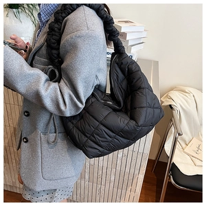 Detail of black quilted puffer tote bag featuring stylish ruffled shoulder strap design