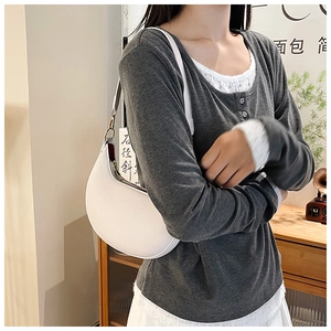 Detail view of a white crescent shoulder bag shown on a model in a cozy interior setting