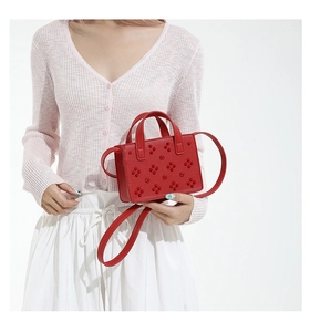 Détail du sac rouge avec des rivets floraux et des poignées supérieures structurées
