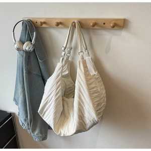 Detail view of cream nylon dumpling bag featuring textured horizontal pleats and soft design