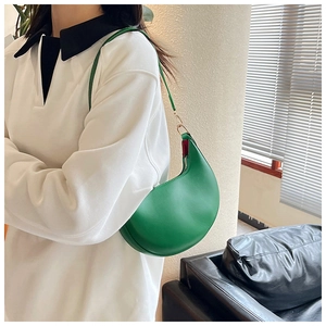 Close-up of green crescent shoulder bag with gold hardware worn on white outfit