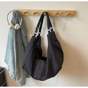 Detail of black pleated nylon hobo bag hanging with a denim jacket and headphones