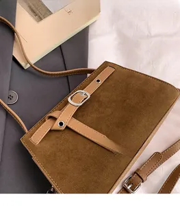 Détail du sac à bandoulière marron mat avec boucle sur une veste de costume grise