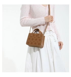 Détail du sac bandoulière en cuir marron avec rivets fleurs 3D porté sur un cardigan rose