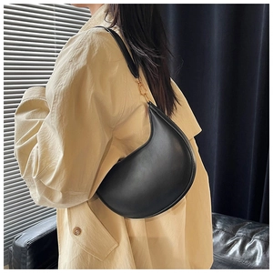 Detail view of a black crescent moon shoulder bag worn with a beige trench coat