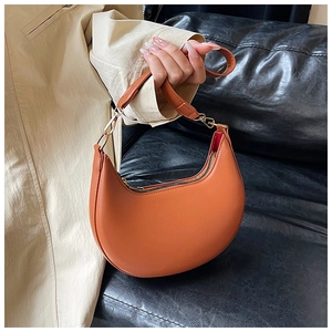 Detail view of the smooth orange crescent bag with golden zippers and adjustable handle