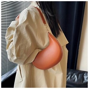 Close-up of orange crescent moon bag with golden metal hardware and slim leather strap