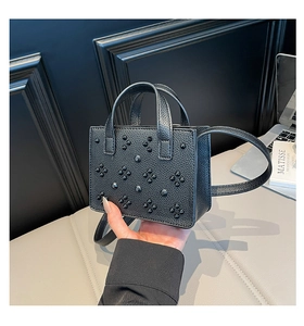 Détail d'un sac à main noir en cuir grainé avec des clous pointus de style punk et poignées