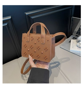 Détail d'un sac cabas en cuir marron à motif litchi avec rivets décoratifs et deux poignées