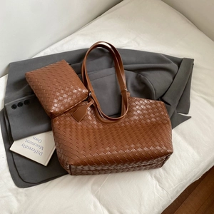 Detail of a brown woven leather tote and matching pouch set on a white bed