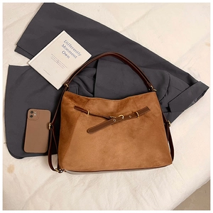 Close-up of brown suede shoulder bag with gold hardware ring on dark grey suit jacket