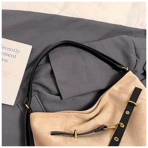 Detailed close-up of khaki suede shoulder bag with black straps and golden metal rings