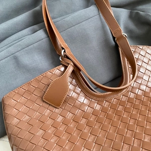 Detail of brown woven tote bag showing Intrecciato craft and minimalist leather texture