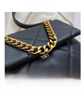 Detailopname van zwart gewatteerd leer met een dikke gouden ketting en metalen sluiting