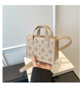 Détail du sac beige en cuir grainé avec rivets ronds et poignées de transport