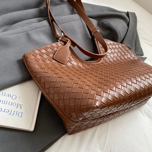 Detailed view of brown woven leather tote bag texture and flat shoulder strap design