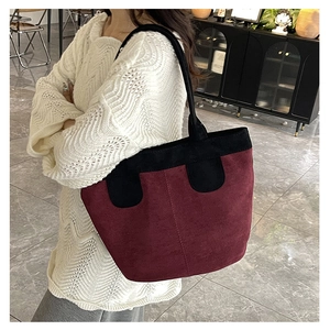Side view of burgundy suede tote bag with black strap on shoulder in interior setting