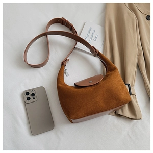Détail d'un sac demi-lune en daim marron caramel avec bandoulière sur tissu blanc pur