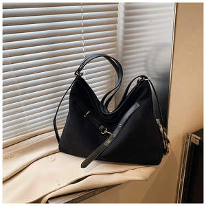 Close-up of black matte suede shoulder bag with gold metal eyelets on beige trench coat