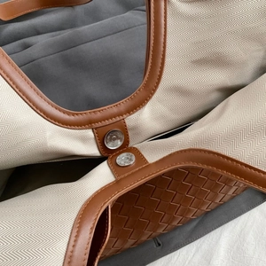 Close-up of herringbone canvas texture, brown leather trim and silver magnetic clasp