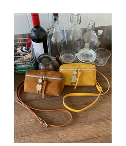 Detail of suede small crossbody bags with a metal robot pendant on a wooden surface